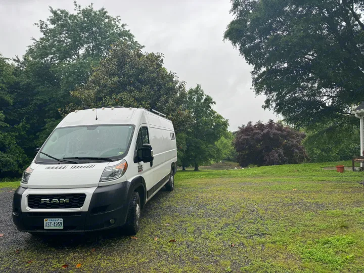 This white Ram ProMaster campervan, an RV rental, is parked on gravel in a lush, cloudy natural setting.. Custom Ram Promaster 2021