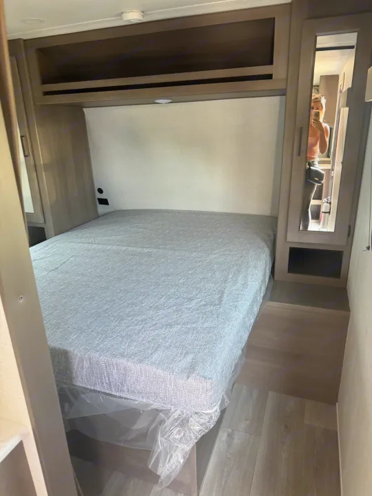 RV rental interior: bedroom with a fresh bed, overhead cabinets, and mirrored closet. Ideal for travel.. Grand Design Transcend Xplor 2024
