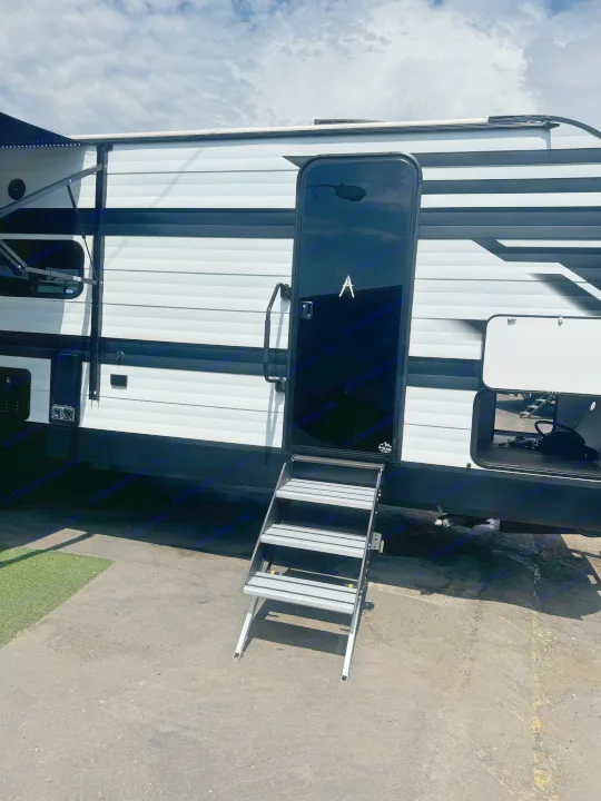 Exterior view of a modern RV rental, featuring tri-fold steps, open storage bays, and a side awning.. Grand Design Transcend Xplor 2024
