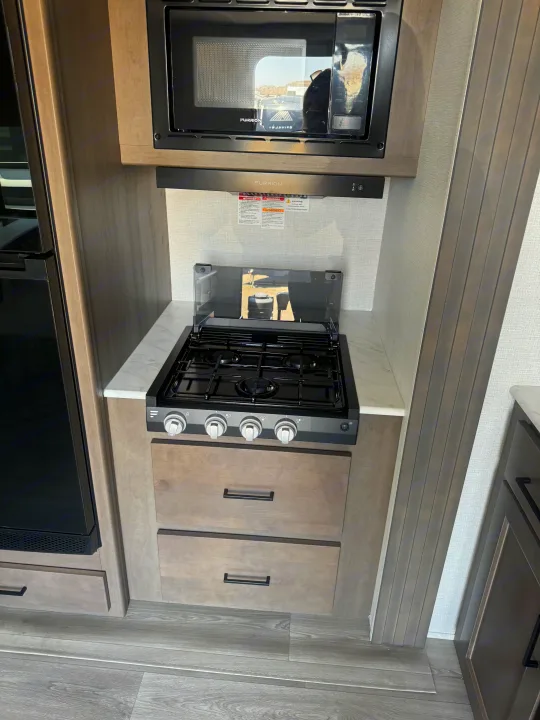 This RV rental kitchen boasts a Furrion microwave, 4-burner gas stove, and ample storage for your travels.. Grand Design Transcend Xplor 2024