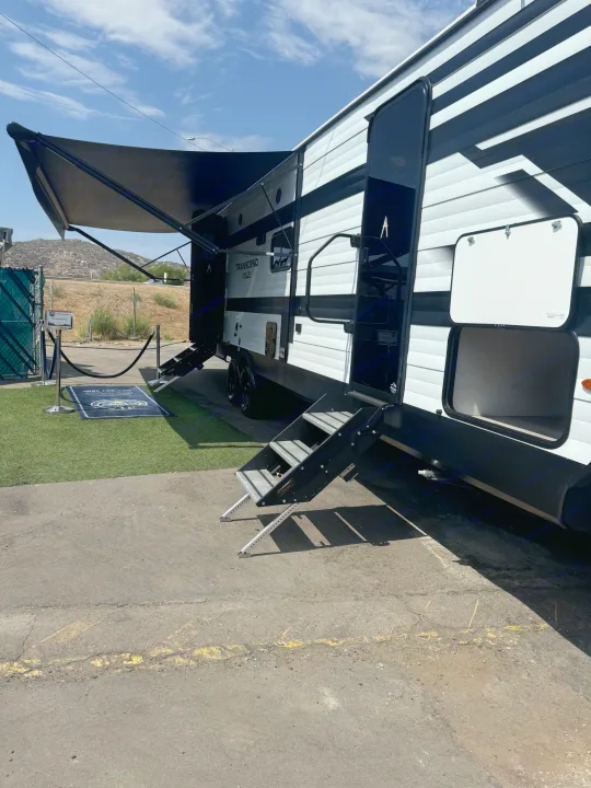 Experience comfort: this white and black RV rental stands ready with its awning out & steps deployed for easy access.. Grand Design Transcend Xplor 2024