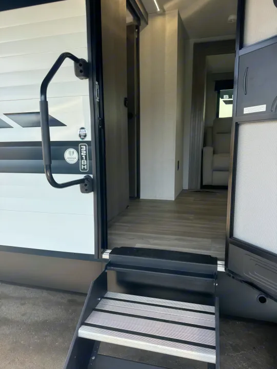 Open RV rental door with entry steps and grab handle, offering a glimpse into the spacious, modern interior.. Grand Design Transcend Xplor 2024