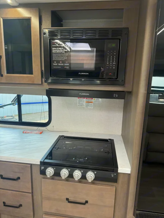 RV rental kitchen: Furrion microwave with air fryer, cooktop, & cabinets. Modern, compact appliances for travel.. Grand Design Transcend Xplor 2024