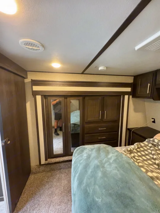 Inside a spacious RV rental bedroom featuring a mirrored wardrobe, plush bed with blankets, ceiling vent, and lights.. Keystone Raptor 2020