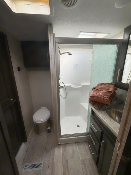 Compact and modern RV rental bathroom with shower, toilet, sink vanity, and storage cabinets.. Keystone Raptor 2020