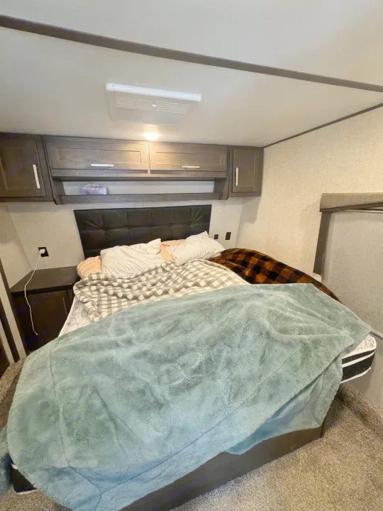 A comfortable RV rental bedroom with a bed, plush blankets, pillows, and ample overhead storage cabinets.. Keystone Raptor 2020