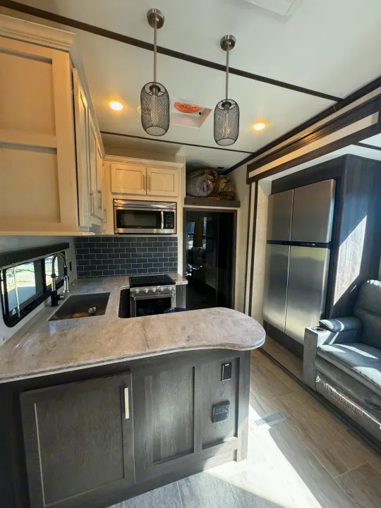 Modern RV rental kitchen featuring stainless steel appliances, sleek cabinetry, and a comfortable living area visible.. Keystone Raptor 2020