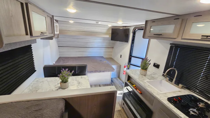 Spacious RV rental interior featuring a bed, dining area, and kitchenette with sink and stovetop.. Coleman 17b 2024