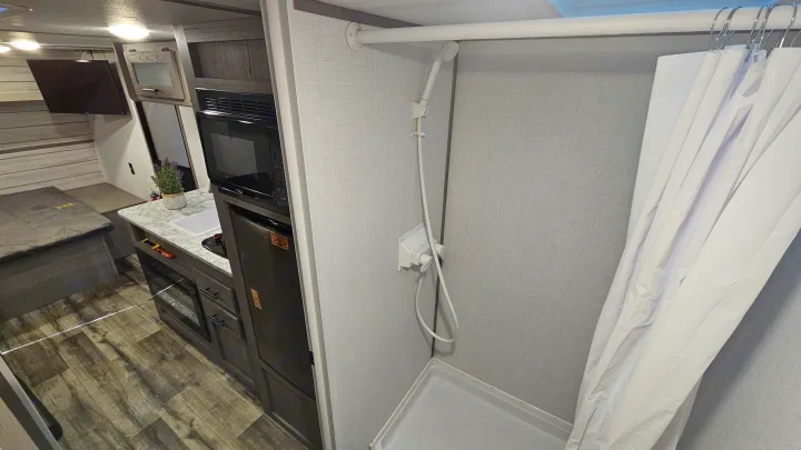RV rental: View of compact kitchen (microwave, fridge, sink) and adjacent shower stall with curtain and pan.. Coleman 17b 2024