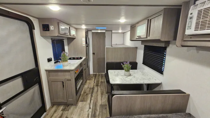 Modern RV rental interior showing a compact kitchen, dining dinette, and bunk beds. Bright and functional living space for adventure.. Coleman 17b 2024