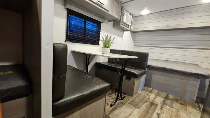 RV rental interior: A compact dinette, bunk bed, window, and AC unit create a cozy travel living space.. Coleman 17b 2024