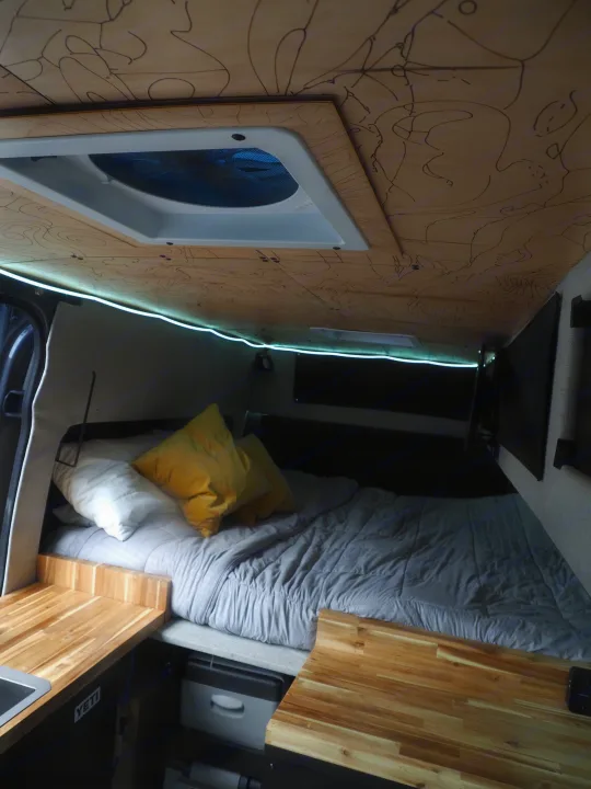 Cozy RV rental interior: bed with pillows, wooden counters, and a map-patterned ceiling with LED lights.. Mercedes Sprinter 2016