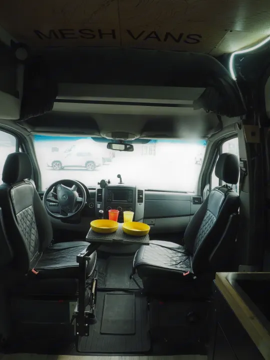 Inside an rv rental camper van: driver's area, comfortable seats, and a center table with bowls. Custom Mesh Vans ceiling design.. Mercedes Sprinter 2016