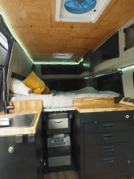 Explore this modern rv rental camper van interior: a comfy bed, kitchen sink, and integrated fridge/storage unit.. Mercedes Sprinter 2016