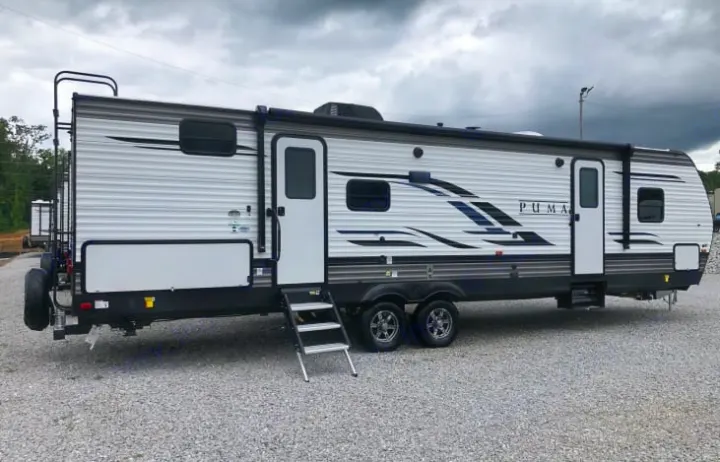 Full view of a white and gray Puma travel trailer RV rental on a gravel lot, ready for your next adventure.. Palomino Puma 2022