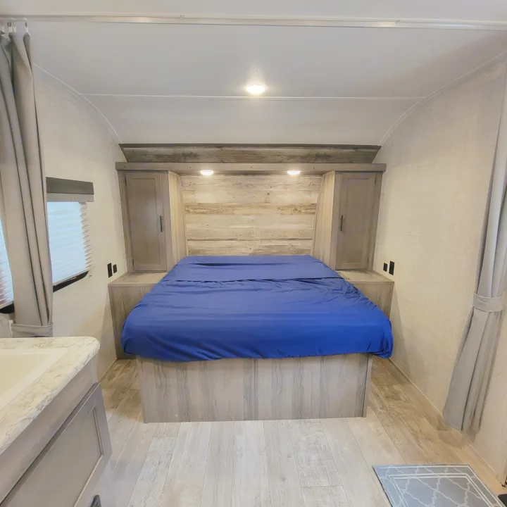 Cozy rv rental bedroom featuring a blue bed, built-in storage, and wood-paneled walls. Perfect for your next adventure.. Gulf Stream Kingsport 2020