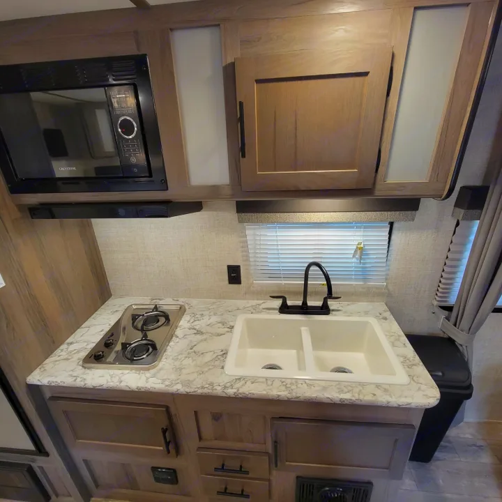 Compact RV rental kitchen with microwave, two-burner stove, double sink, and light countertop.. Gulf Stream Kingsport 2020