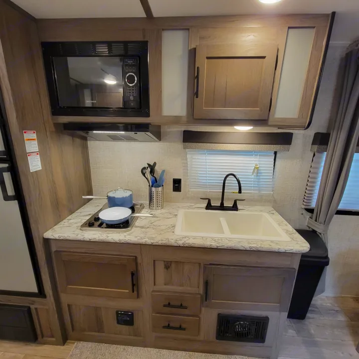 This RV rental kitchen features a microwave, two-burner stove, sink, and ample cabinet storage.. Gulf Stream Kingsport 2020