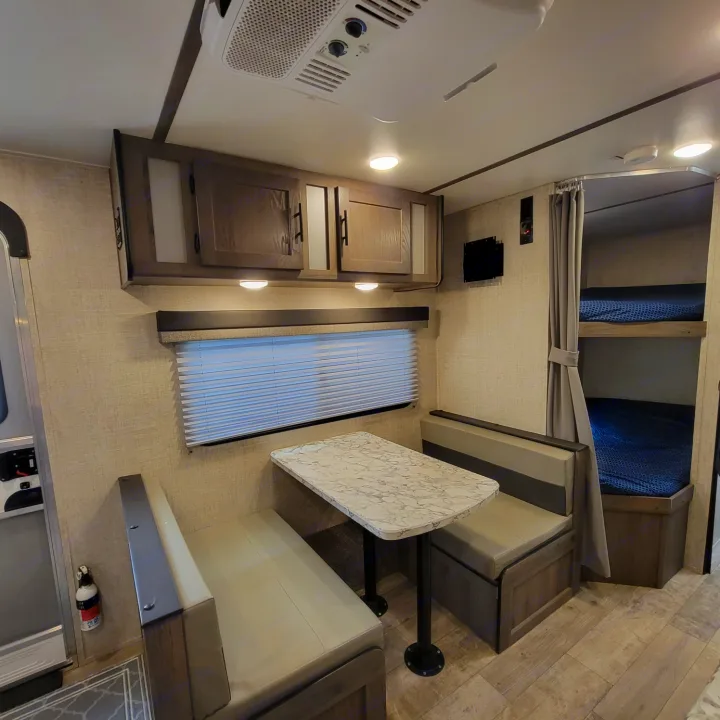 Inside an RV rental: a modern dinette with overhead storage, a window, and private bunk beds, ready for your next adventure.. Gulf Stream Kingsport 2020