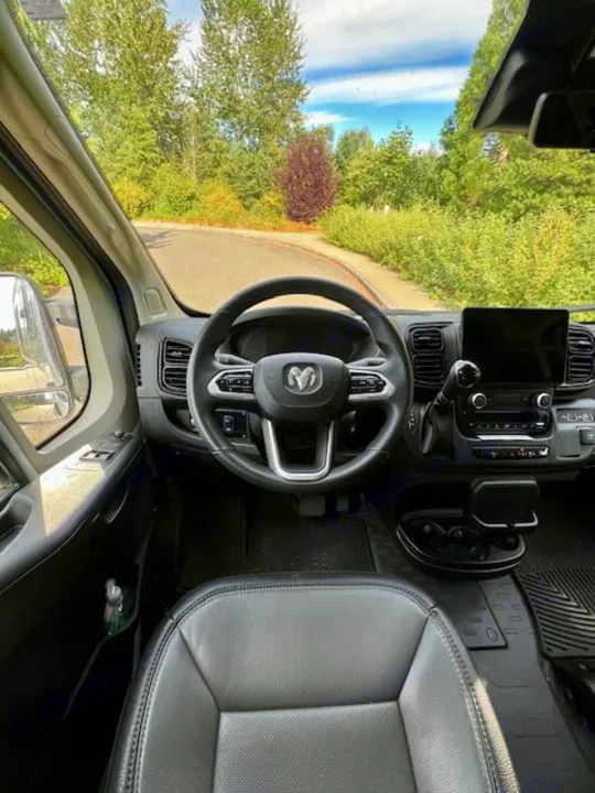 Driver's view of a spacious RV rental interior: Ram steering wheel, dash, and winding road ahead.. Winnebago Winnebago 2023