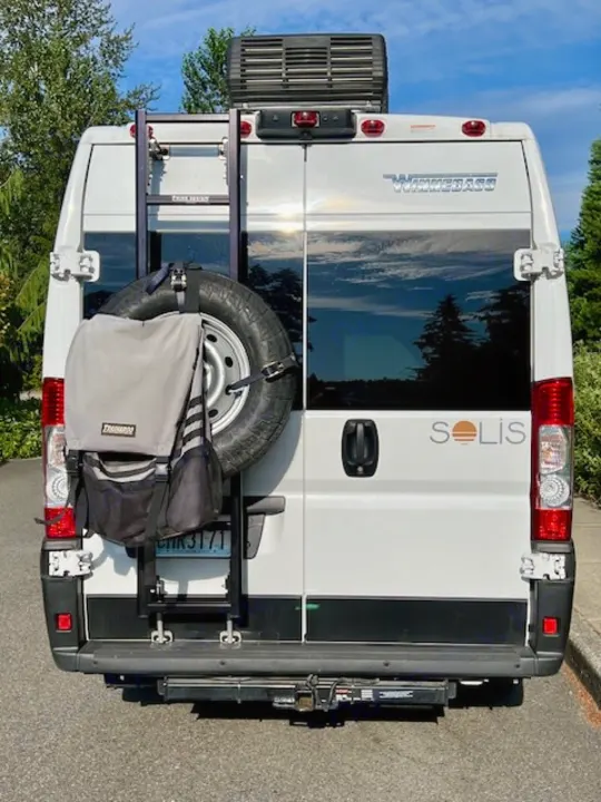 Explore van life! This Winnebago Solis RV rental shows its rear with spare tire, ladder, and hitch.. Winnebago Winnebago 2023