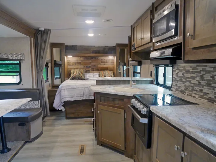 Spacious RV rental interior featuring a modern kitchen, comfortable bedroom with wood accent wall, and a dining area.. Dutchmen Aspen Trail 2020