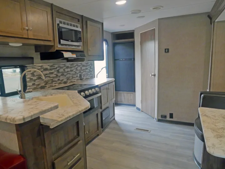 Bright RV rental interior featuring a modern kitchen with appliances, ample counter space, and a dining area.. Dutchmen Aspen Trail 2020