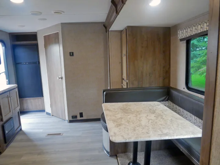 A bright RV rental interior featuring a dinette with a patterned bench, light countertop, and integrated refrigerator.. Dutchmen Aspen Trail 2020