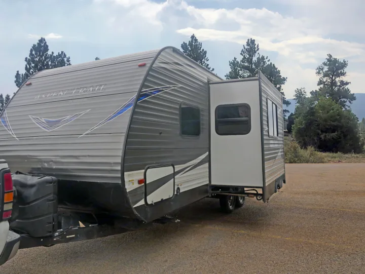 Gray Aspen Trail RV rental with extended slide-out, parked on gravel. Ready for your next outdoor road trip adventure!. Dutchmen Aspen Trail 2020