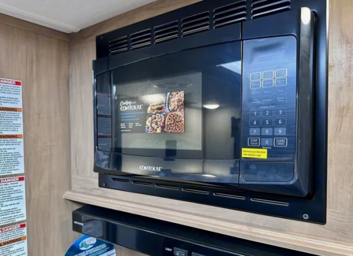 A modern black Contoure microwave, installed in an RV rental kitchen, is ready for quick meals on the go.. Forest River Cherokee Grey Wolf 2023