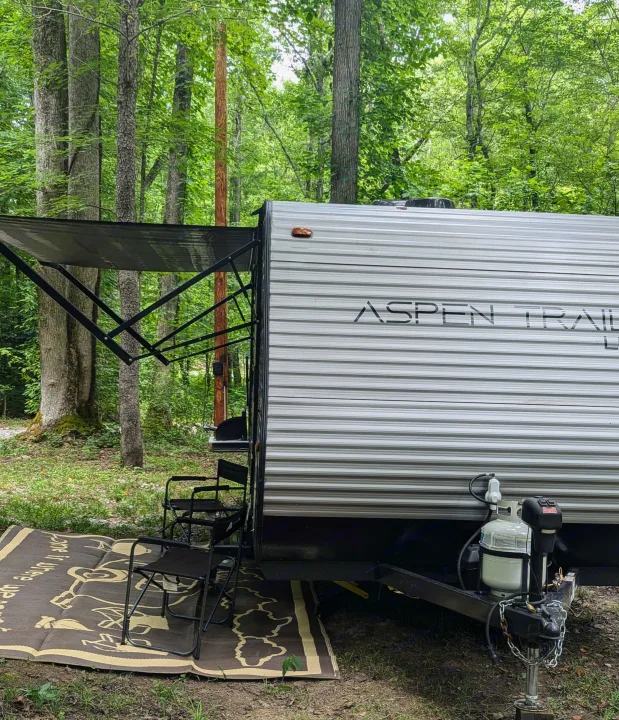 RV rental: Aspen Trail travel trailer parked at a wooded campsite, with awning extended over outdoor mat and chairs.. Aspen Trail LE 2022