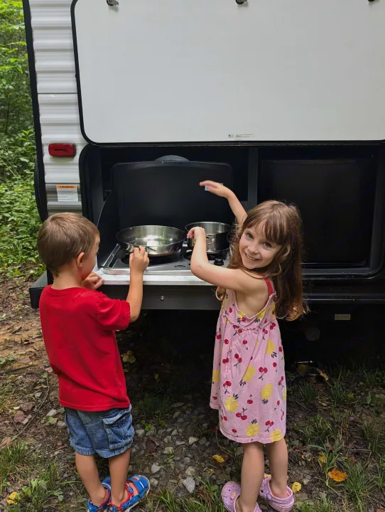 Two kids delight in outdoor cooking from their RV rental. Family fun at the campsite!. Aspen Trail LE 2022