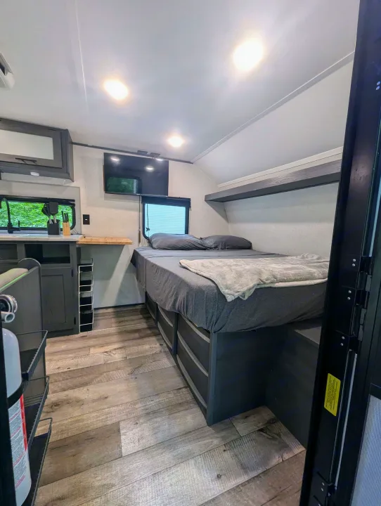 RV rental cozy interior: full bed with storage drawers, shelf, wall-mounted TV, & kitchen. Wood-look floor.. Aspen Trail LE 2022