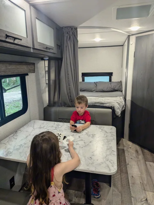 Fun in an rv rental! Two kids play cards at a table inside a modern RV, showing the cozy living and sleeping areas.. Aspen Trail LE 2022