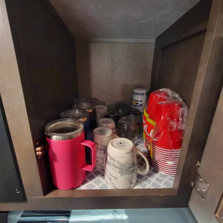Organized RV rental cabinet holds various drinkware: a pink mug, red plastic cups, and ceramic mugs.. Forest River Flagstaff Super Lite 2019