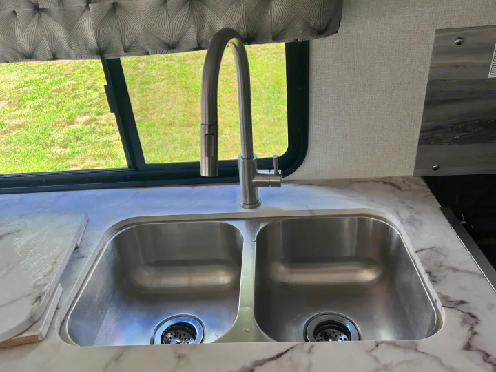 RV rental kitchen with a double sink, modern faucet, marble-look counters, and a window view of green grass.. Forest River Sunseeker Classic 2020