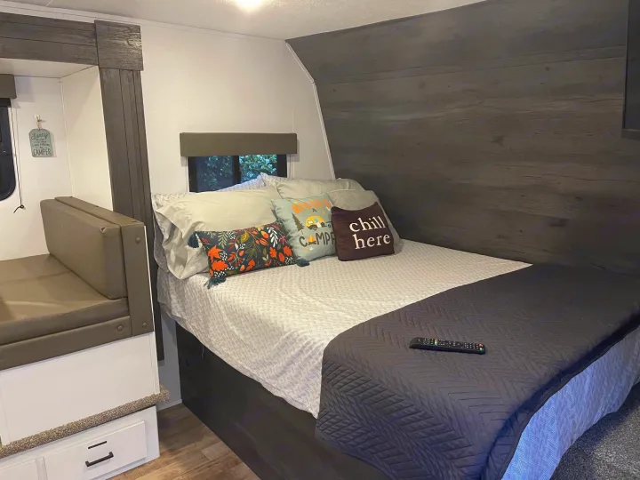 Relaxing RV rental bedroom features a comfy bed with decorative pillows and built-in dinette seating for a cozy stay.. Keystone RV Hideout 2021