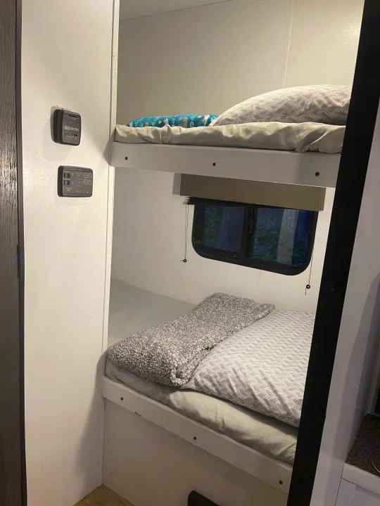 Cozy bunk beds in an RV rental, complete with bedding, a window, and climate controls for comfortable travel.. Keystone RV Hideout 2021