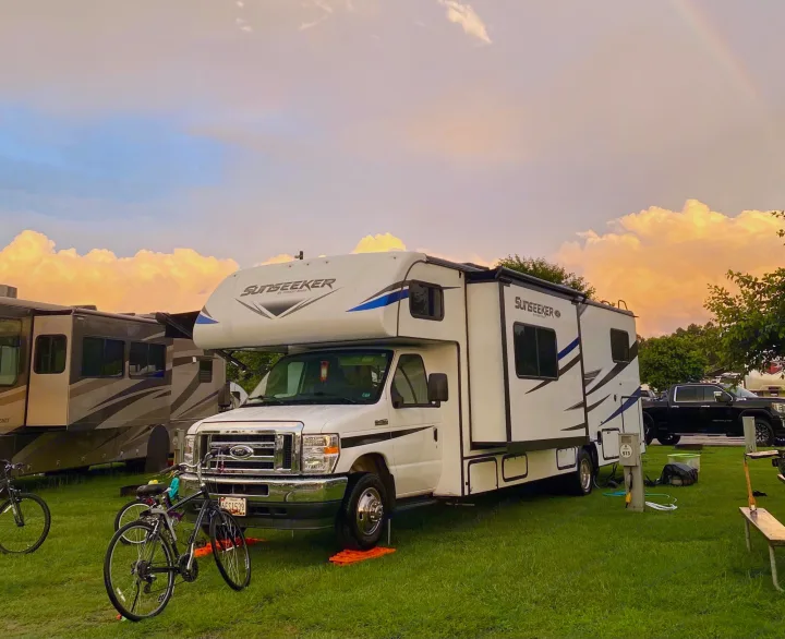 A spacious white rv rental parked at a green campsite, bathed in the warm glow of a sunset sky. Perfect for family trips.. Forest River Sunseeker 3250DSLE 2022