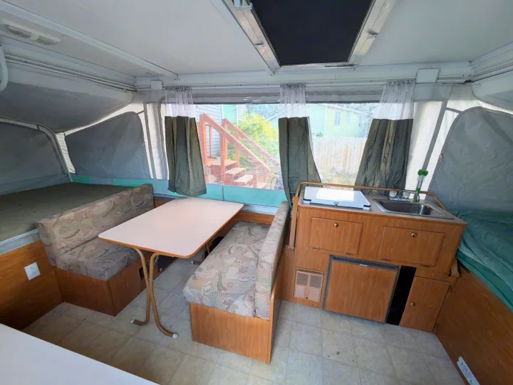Inside this cozy RV rental pop-up camper: dining area, compact kitchen, and two bed sections.. Fleetwood Sedona 2004
