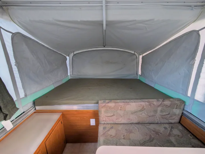 Inside an RV rental pop-up camper, showcasing the spacious bed area, dinette seating, and light-colored canvas walls.. Fleetwood Sedona 2004
