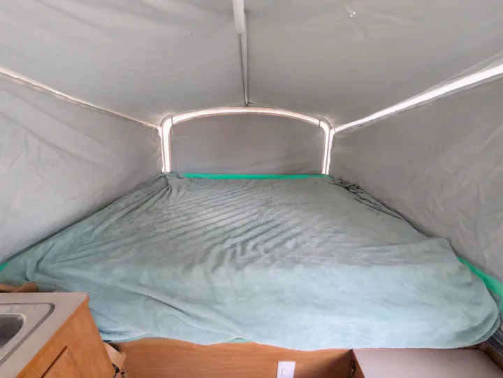 Inside an RV rental pop-up camper, featuring a spacious sleeping area with a soft blanket and bright canvas walls.. Fleetwood Sedona 2004