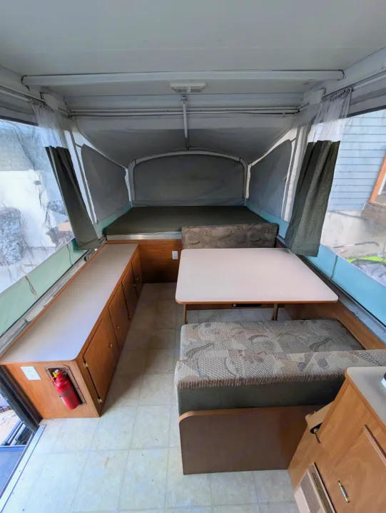 Interior of a pop-up RV rental, featuring a bed, dinette with patterned cushions, and a storage cabinet on the left.. Fleetwood Sedona 2004