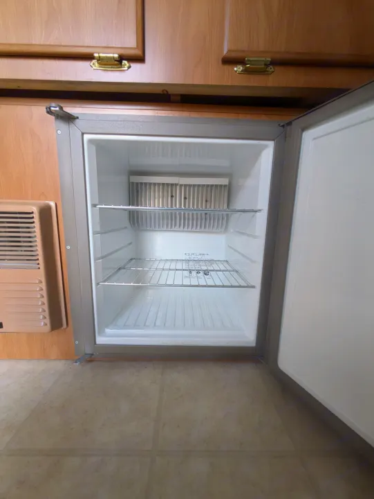 Open Dometic refrigerator in an RV rental, showing empty shelves and interior cooling fins.. Fleetwood Sedona 2004