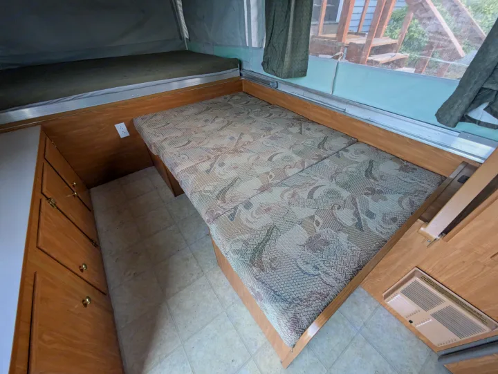 Inside a pop-up RV rental: compact living area with patterned cushions, bunk bed, cabinet, and vent.. Fleetwood Sedona 2004