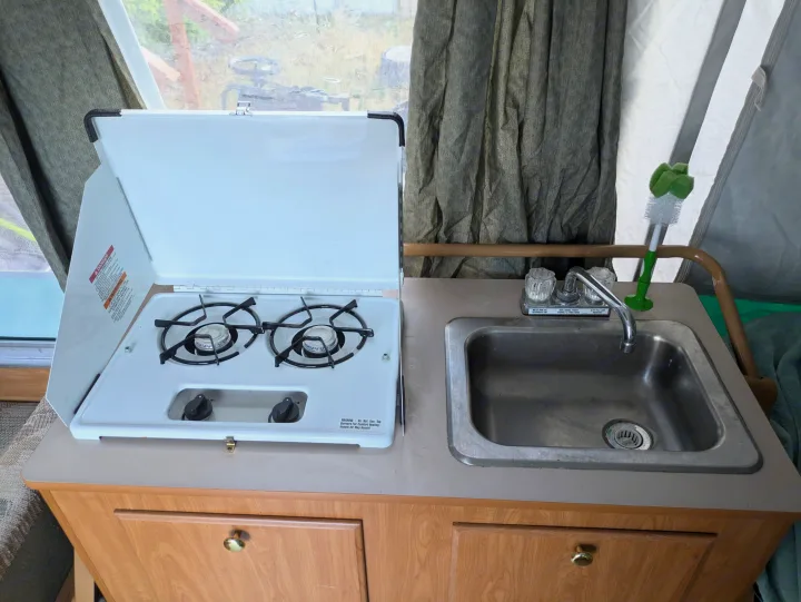 Pop-up RV rental kitchen showing a two-burner stove, stainless steel sink, and storage cabinets below.. Fleetwood Sedona 2004