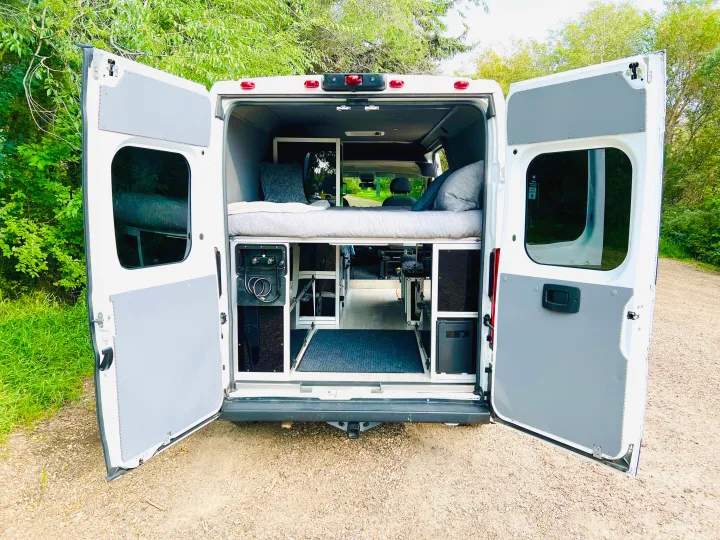 Spacious RV rental with custom interior: open doors revealing a comfy bed, storage, & shower for mobile adventures.. Dodge Promaster 2500 Highroof 2019