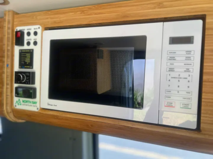 Compact Magic Chef microwave and control panel within a sleek bamboo wood interior of an RV rental.. Mercedes Sprinter Sprinter 2500 2021
