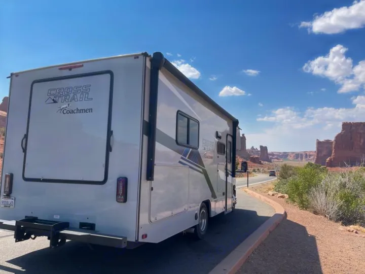 An RV rental parked at a scenic viewpoint, showcasing towering red rock formations in a vast desert landscape under a clear blue sky.. Forest River Coachmen Crosstrail 2023