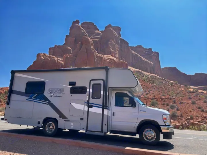RV rental parked before dramatic red rock formations under a clear blue sky, ideal for scenic road trips.. Forest River Coachmen Crosstrail 2023